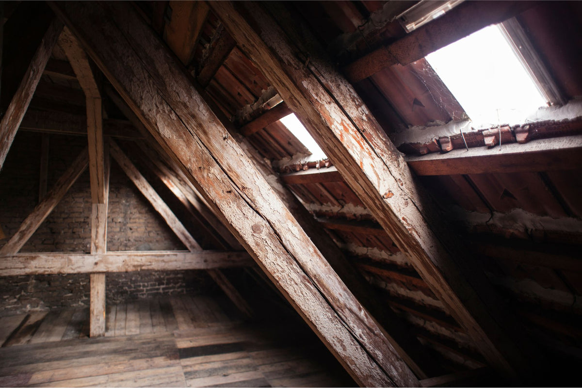 Dachboden mit sichtbaren alten Holzbalken und zwei Dachfenstern, die Tageslicht hereinlassen
