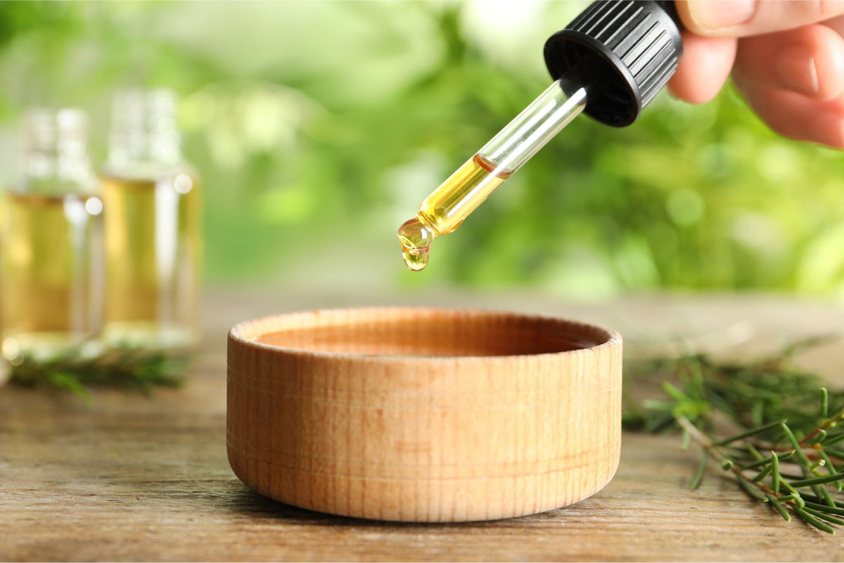 Pipette mit gelbem Öl über einer kleinen Holzschale, im Hintergrund Glasfläschchen und Rosmarinzweige